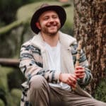 Tom Vogt sitz mit einer Flöte im Wald